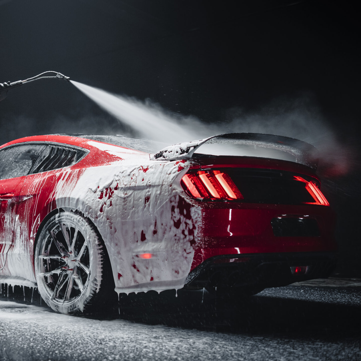Automotive detailer washing away smart soap and foam with a pressure washer.